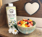 A fruit salad in a small bowl, sitting on a wooden shelf with La Tourangelle's extra virgin olive oil can in the background.