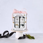 A gift box of two cans of truffle oil, sitting on a cake stand, surrounded by black ribbon and a sprig of rosemary. 